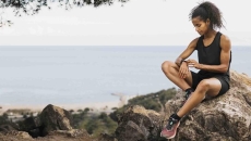 Runner sitting next to the ocean while looking at their smartwatch