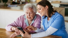 Caregiver with a patient in their home while looking at a phone