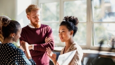 Person in maroon sweater talks with people wearing beige, polka dots