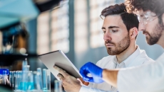 Two scientists in a laboratory setting looking at a tablet while surrounded by beakers