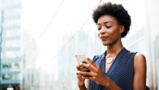 Person standing up looking at their phone with a city in the background