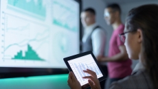 Three people in a room looking at different graphs on separate screens