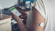 Patient with wearable glucose monitoring device looking at smart phone