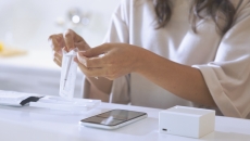 A woman removing the Cue wand from its package with a smartphone and Reader on the table in front of her