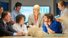 A mixed group of healthcare professionals and business people meet around a conference table.