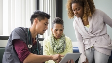 A doctor looking at data on a tablet with a patient and her family member.