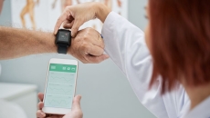 Doctor showing senior patient how to synchronize health app in smartphone and smartwatch