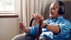 An older man with a cane using a smartphone in his home.
