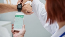 A doctor showing a senior patient how to synchronize their health app in a smartphone and a smartwatch