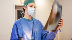 Healthcare provider in scrubs wearing a mask and looking at a large diagnostic image