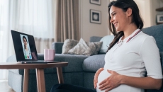 Person sitting on the floor while rubbing their pregnant belly and talking to a healthcare provider on a computer