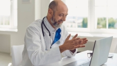 Healthcare provider wearing a lab coat and a stethoscope around their neck while sitting at a desk looking at a computer