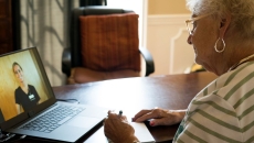 Person sitting at a table with a laptop on it, talking to a healthcare provider via the computer