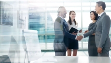 Four people standing in front of a large window with two of them shaking hands