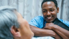 Nurse leaning against a patient's bed while the patient looks at them