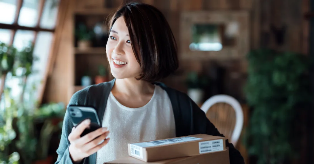 Person standing in their home while holding a phone and surrounded by boxes
