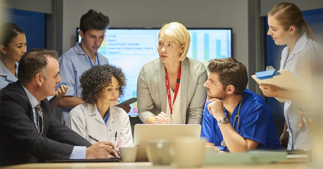 People sitting and standing around a table looking at a computer
