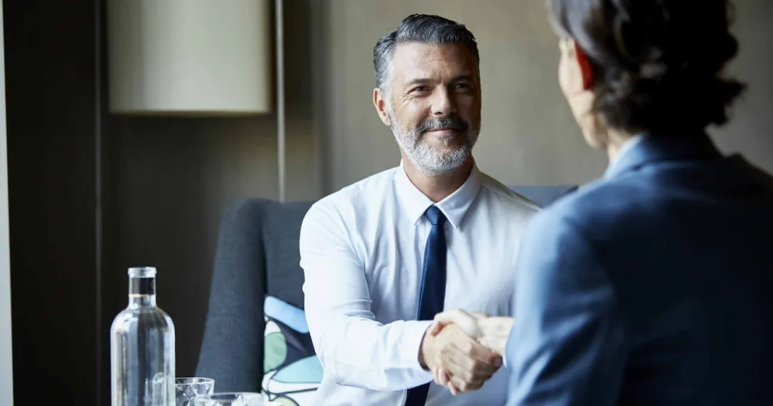 Two people sitting across from each other at a desk shaking hands