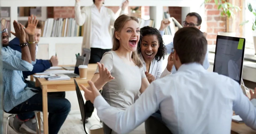 Three people with arms raised celebrating around computer monitor