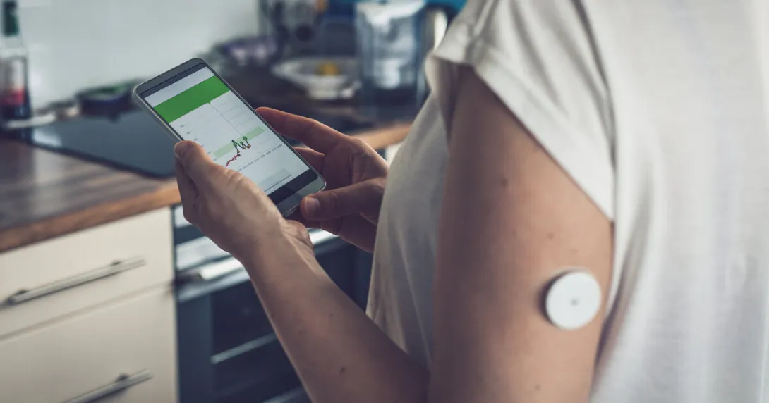 A patient with a wearable sensor patch checking their blood glucose level through a mobile app