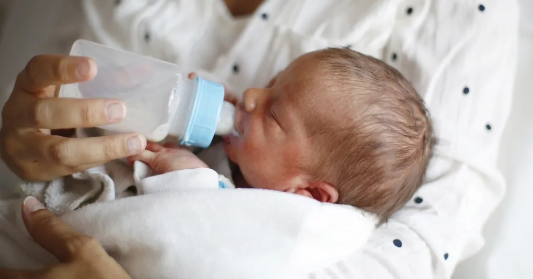 Person holding another small person while feeding them with a bottle