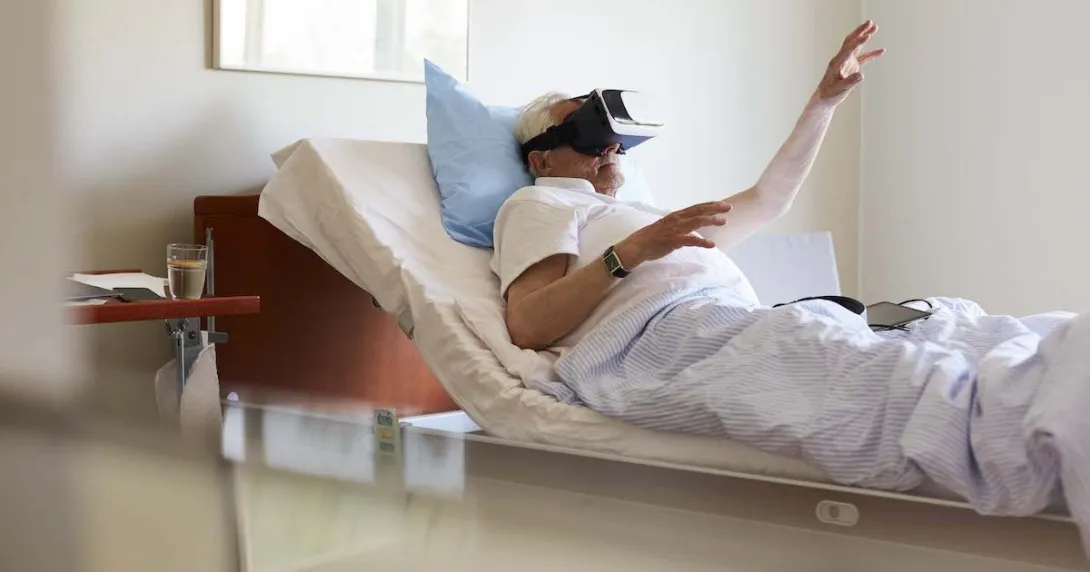 Person in a clinical setting lying in bed with their hand raised while wearing a virtual reality headset