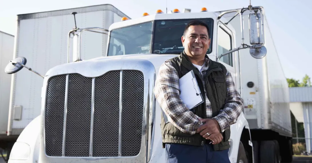 Truck driver standing in front of a semi-truck while holding a clipboard