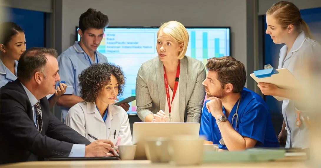 A mixed group of healthcare professionals and business people meet around a conference table.