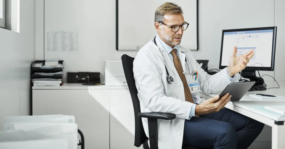 A doctor using a tablet at his desk in a clinic.
