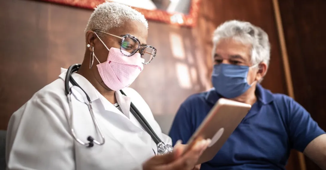 A doctor holding a tablet while talking to a patient.