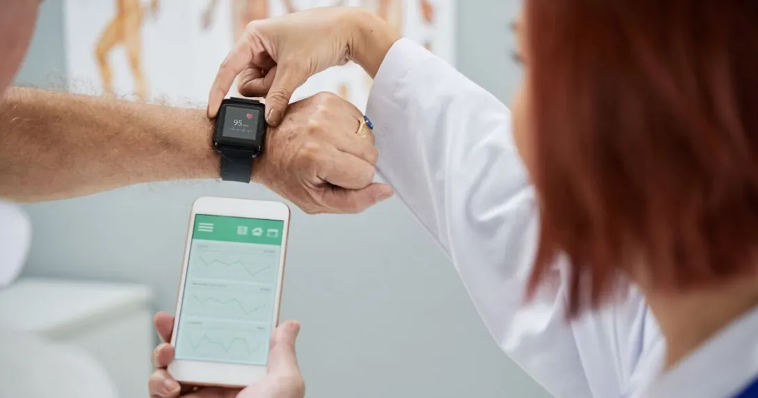 A doctor helping a patient sync heart rate data from a wearable to a smartphone.