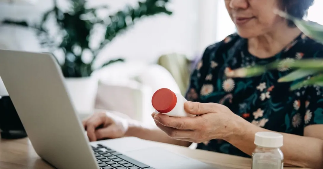 Person holding a prescription bottle while using a laptop
