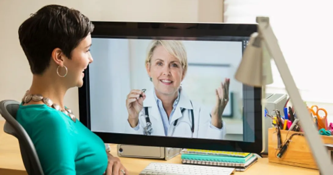 Person with green shirt talks with person on computer monitor in lab coat