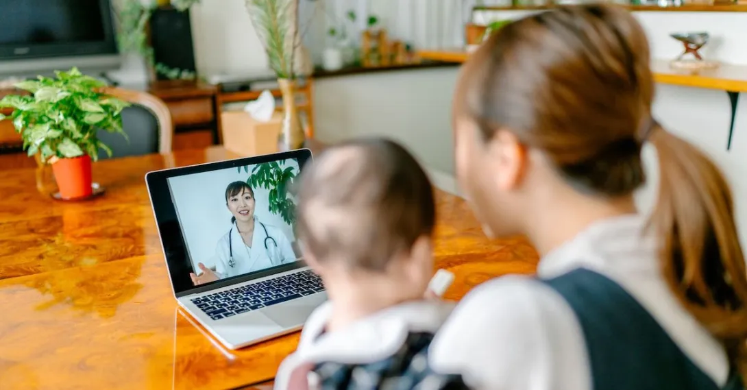 A mom holding a baby talking to a doctor via telehealth