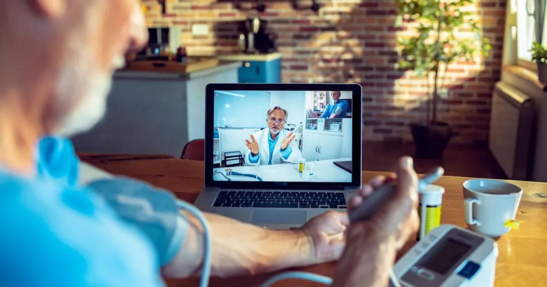 An older man talking to a provider via telehealth while checking his blood pressure
