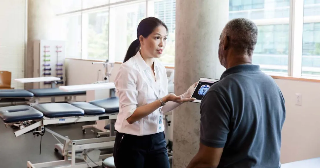 A medical professional uses a digital tablet to explain brain injury and recovery to a person after his stroke.