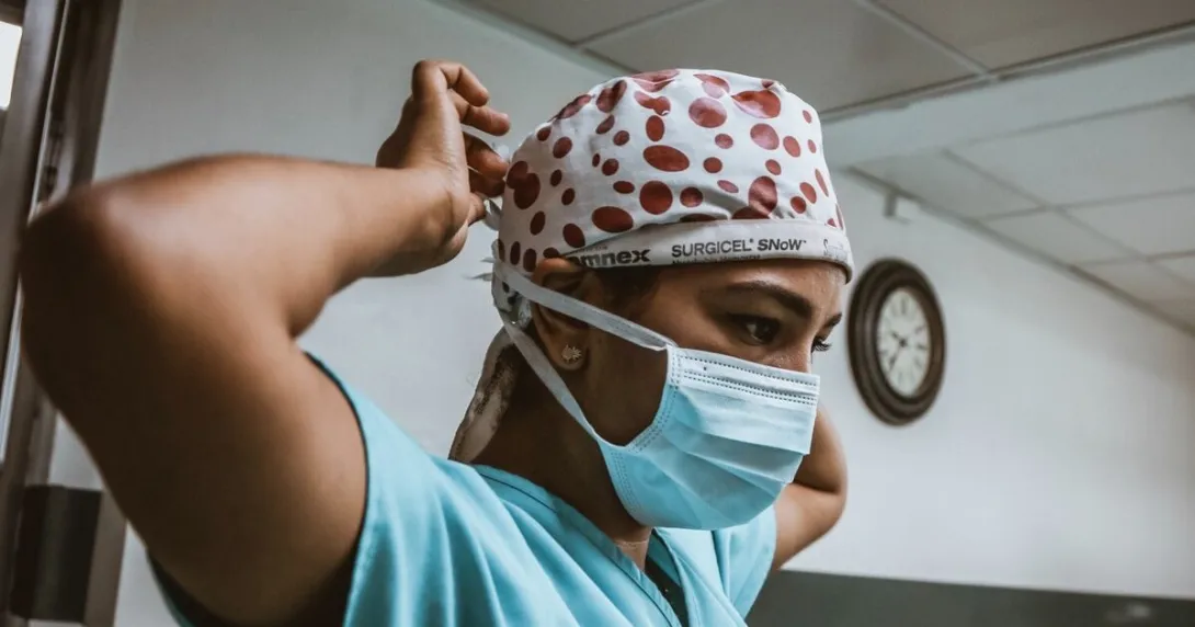 A health worker wearing a surgical mask ties their head cap
