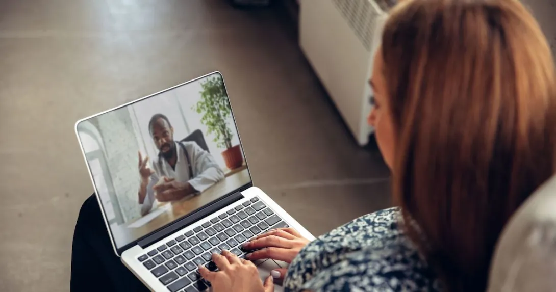 A woman talking to a doctor via telehealth using her laptop