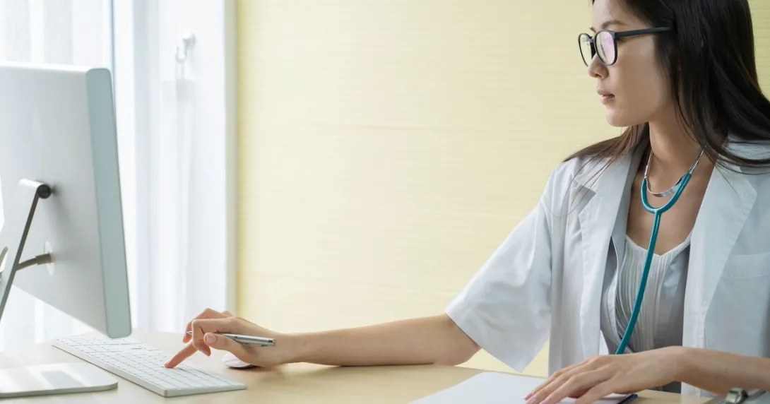 Healthcare provider sitting at a desk wearing a stethoscope around their neck and working on a computer