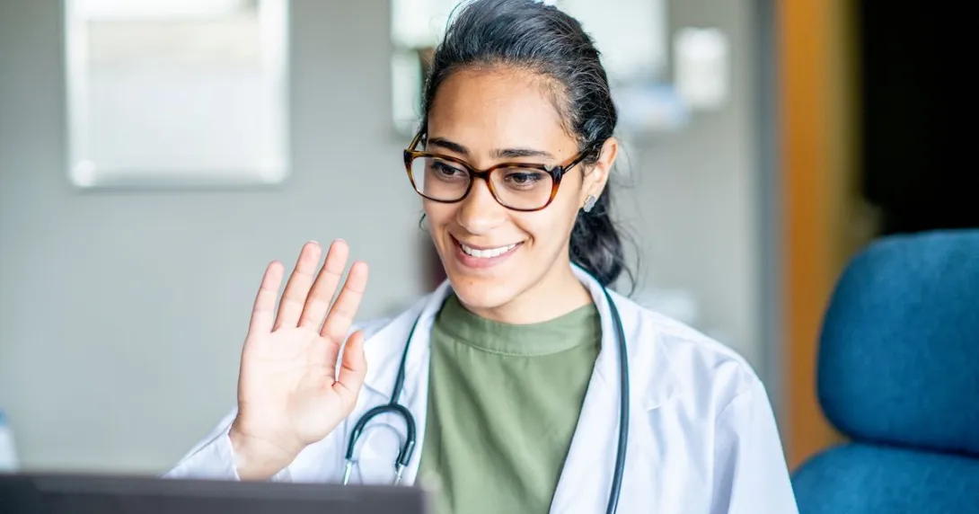Healthcare provider sitting in front of a computer waving at the screen