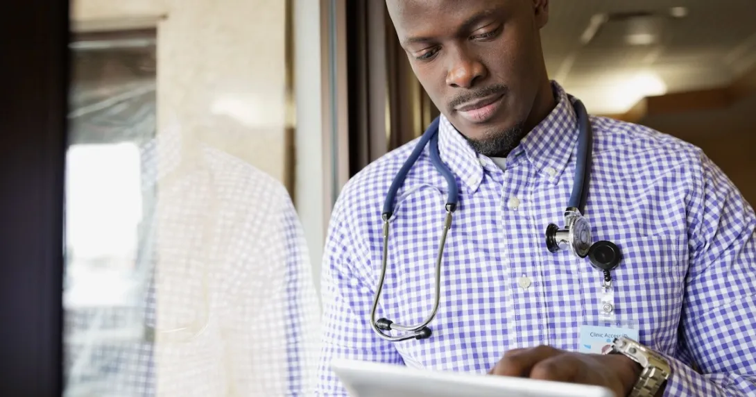 Healthcare provider standing next to a window while looking at a tablet
