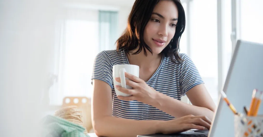 Person sitting at their computer while holding a cup of coffee