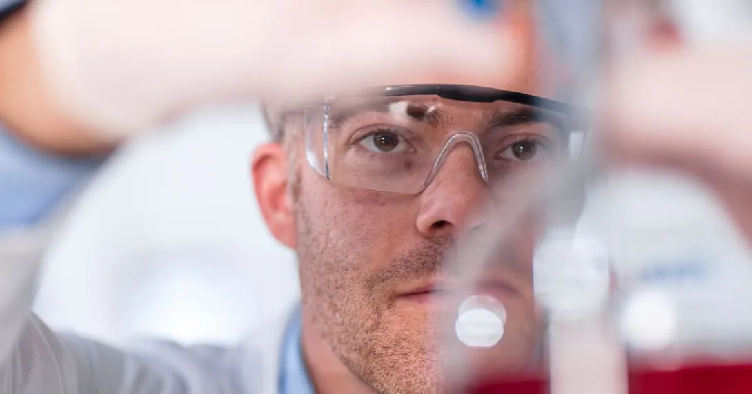 Scientist in a laboratory wearing safety goggles and putting something in a beaker