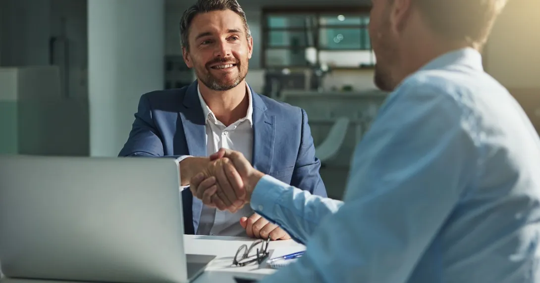 Two people sitting across from each other at a table and shaking hands