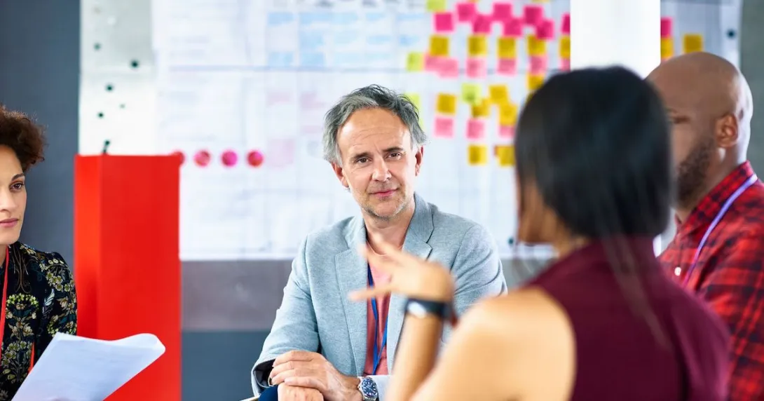 People sitting around a table in front of a whiteboard talking to each other