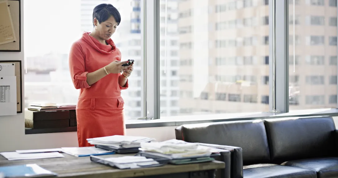 A person standing at her desk using a smartphone.