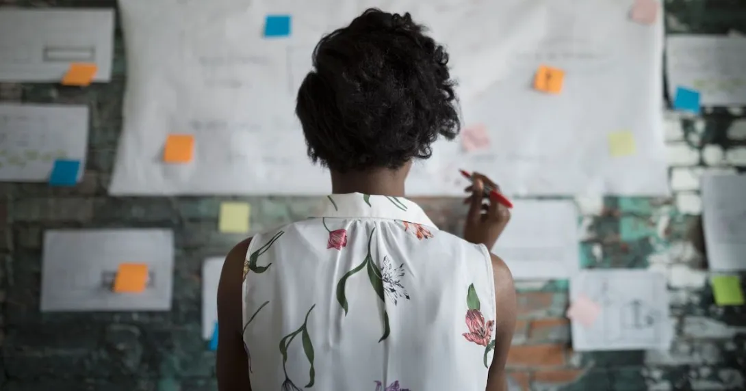 A woman standing with her back to the camera before a wall covered in planning documents and post-it notes